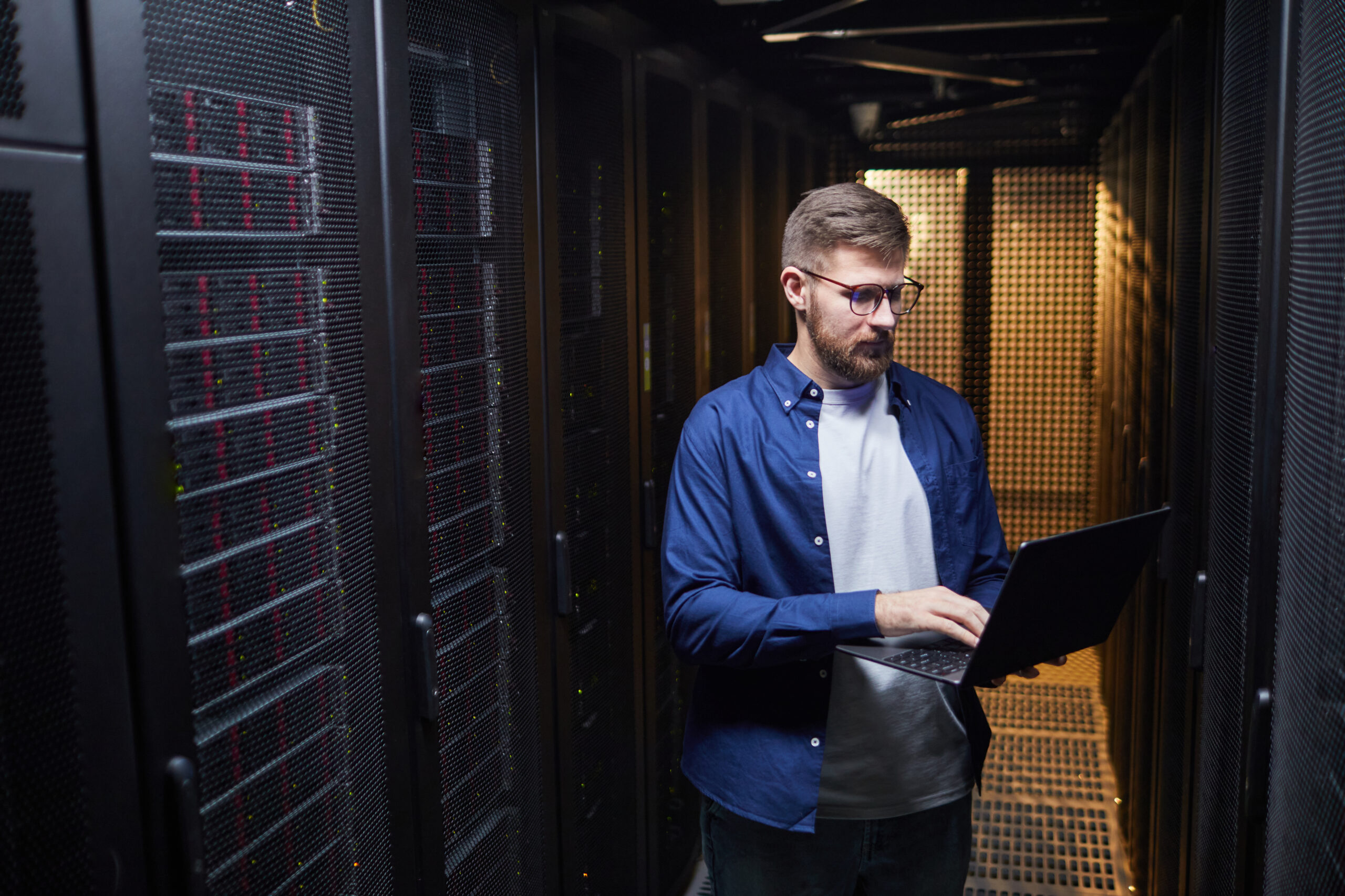 IT professional working in a server room managing hardware and software with focused expression. Surrounded by server racks filled with equipment, creating tech-focused environment
